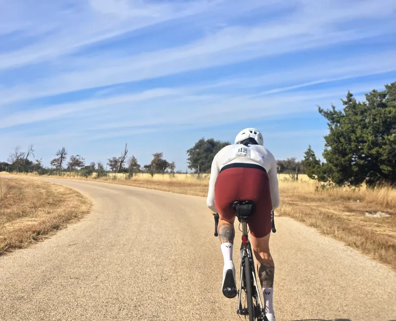 A rider in a white and maroon kit on a curving open road under a wispy sky.