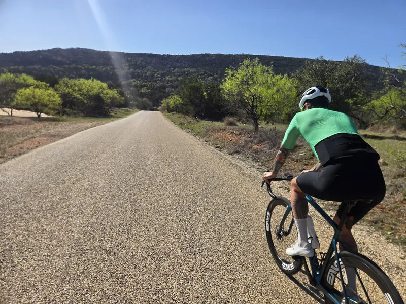 A rider in a mint jersey on a road heading toward a green hill.