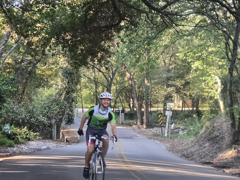 A smiling rider in a green jersey rolling under a tunnel of trees.