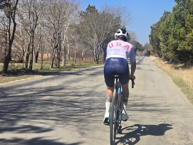 A rider in a USA jersey on a country road lined with trees.